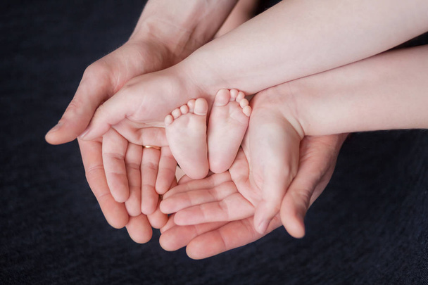 hands of parents hold the feet of a newborn baby, pink heels in their palms, parental love - Фото, изображение