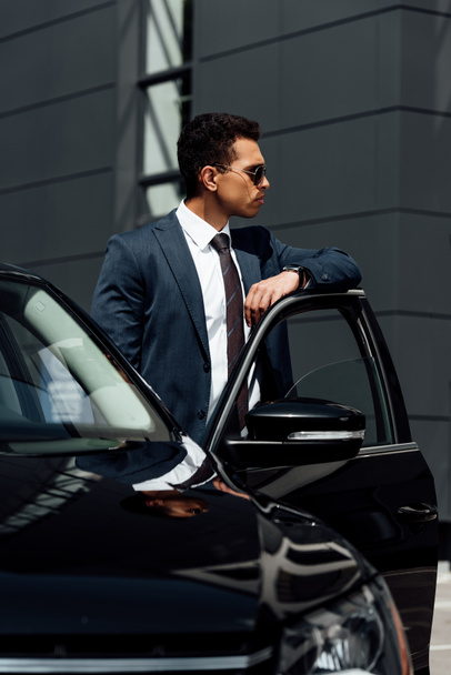 african american businessman in suit and sunglasses standing near car at sunny day - Valokuva, kuva