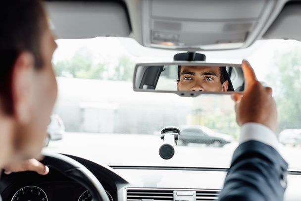Afro-Amerikaanse zakenman in pak rijden auto en kijken naar spiegel - Foto, afbeelding