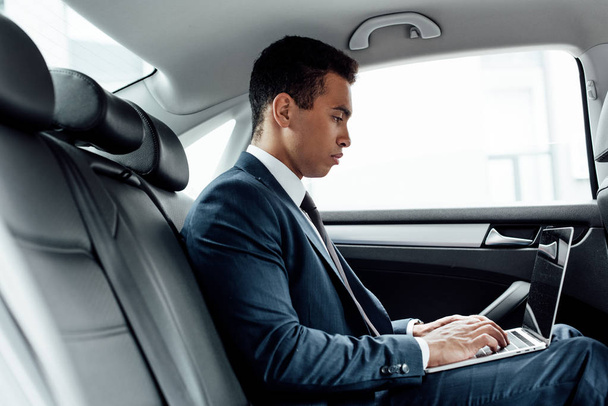 side view of african american businessman using laptop in car - Valokuva, kuva