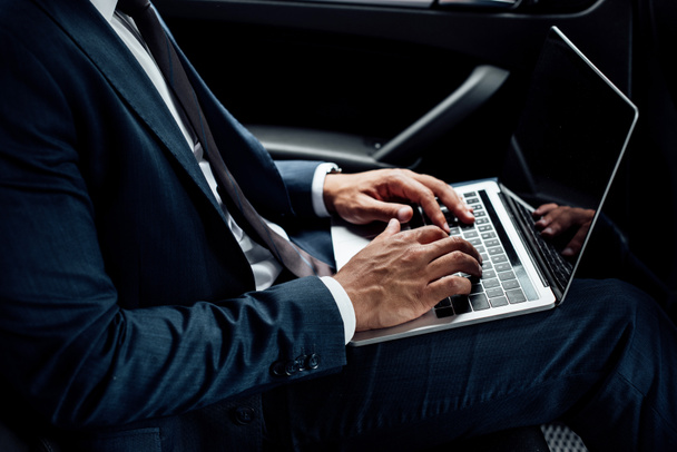 partial view of african american businessman using laptop in car - Photo, Image