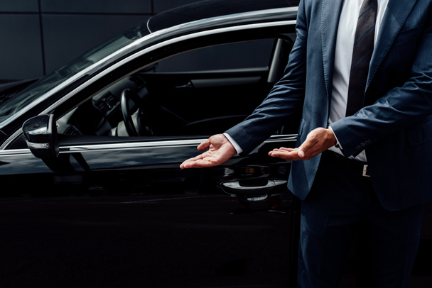 cropped view of african american man in suit pointing at black car door - Foto, imagen