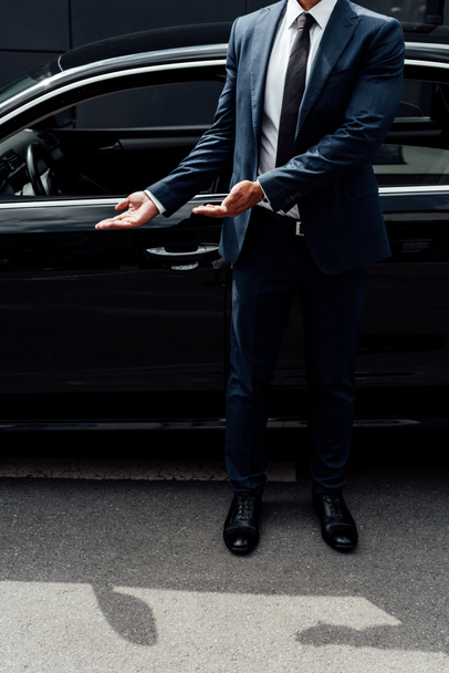 Teilansicht eines Afroamerikaners im Anzug, der mit den Händen auf die Autotür zeigt - Foto, Bild