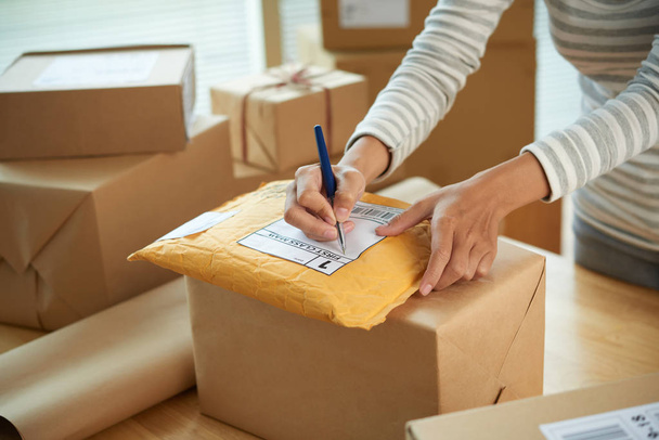 Handen van vrouw schrijven adres op eerste klas pakket met goederen - Foto, afbeelding