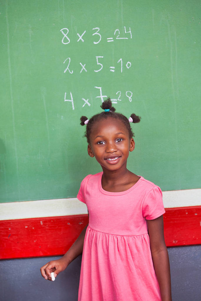 Nuori afrikkalainen tyttö koulussa tekee matematiikkaa liitutaulussa
 - Valokuva, kuva