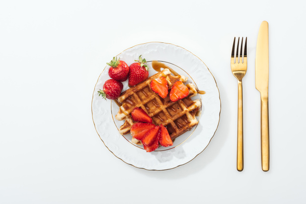 top view of plate with waffle and strawberries near fork and knife on white - Photo, Image