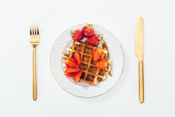top view of waffle and strawberries on plate and fork with knife near plate  - Foto, Bild