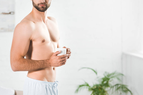 Cropped view of shirtless man holding cup of coffee at home in morning - Фото, изображение