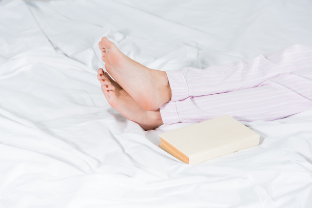 Oříznutý pohled člověka v pyžamu, který ležel v posteli u knihy - Fotografie, Obrázek
