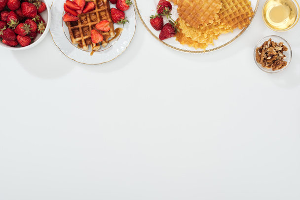 top view of waffles and strawberries on plated near bowls with honey and nuts on white - Fotoğraf, Görsel