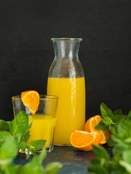 Healthy fruit drink. Natural fresh squeezed orange or tangerine juice in a glass bottle with water drops and fresh green mint on a dark background. - Fotoğraf, Görsel