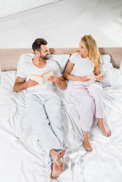 beautiful smiling couple lying in bed with books at home  - Fotoğraf, Görsel