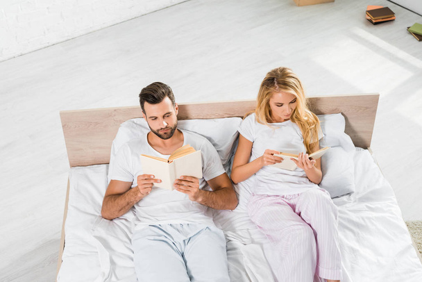 high angle view of beautiful couple lying in bed with books at home  - Foto, afbeelding