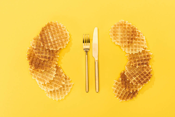 top view of waffles near golden fork and knife on yellow - Foto, Bild