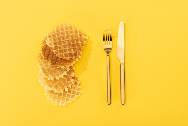 top view of crispy and delicious waffles near cutlery on yellow - 写真・画像