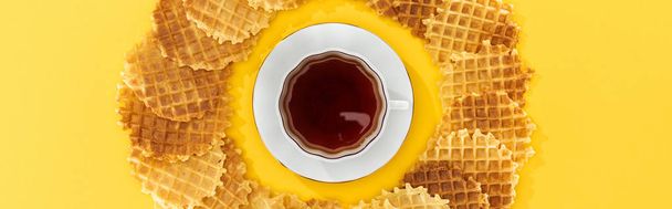 panoramiczny strzał gofry w kręgu z filiżanką herbaty w środku na żółtym - Zdjęcie, obraz