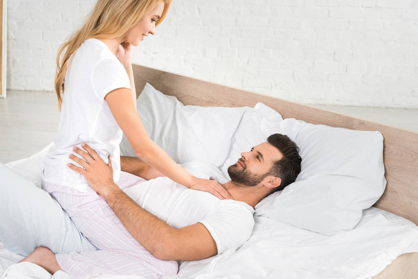 自宅でベッドで抱きしめるパジャマの美しいカップル - 写真・画像