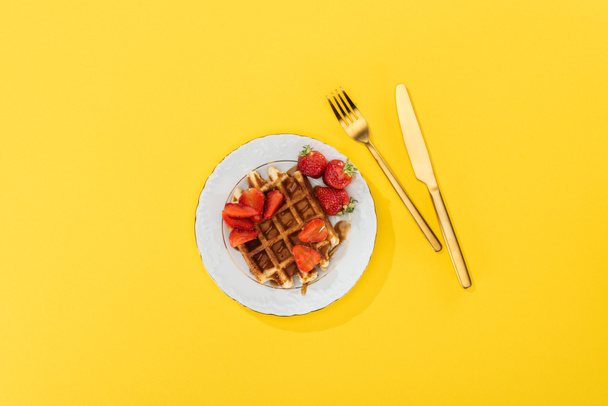 top view of plate with tasty waffle and strawberries for breakfast on yellow  - Фото, зображення