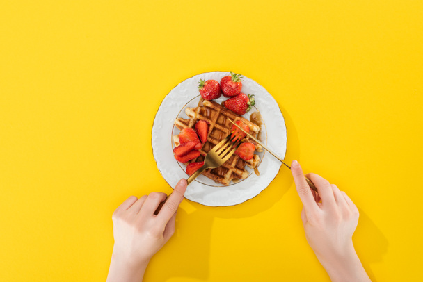 cropped view of woman cutting waffle on plate on yellow - 写真・画像