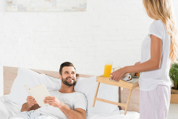woman bringing breakfast to happy man in bed in morning - Фото, зображення