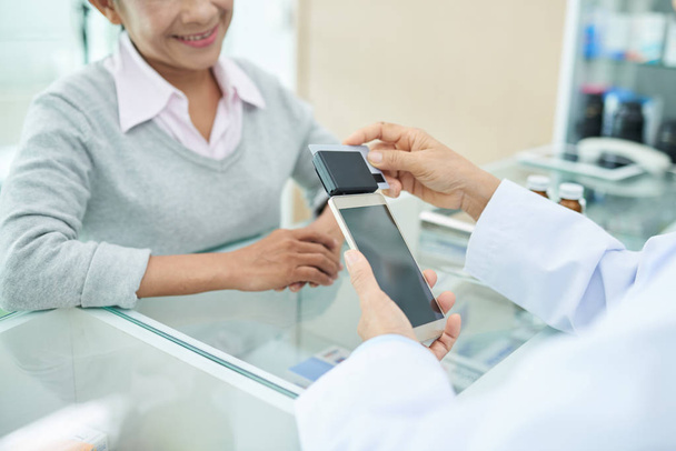 Farmacéutico usando lector de tarjetas conectado a smartphone para aceptar pago
 - Foto, imagen