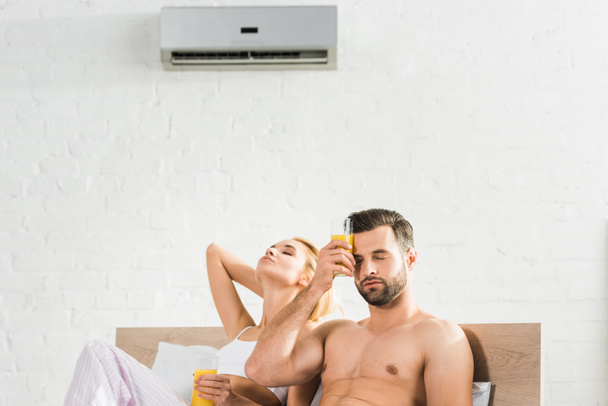 pareja con zumo de naranja sufriendo de calor bajo el aire acondicionado en la cama en casa
 - Foto, Imagen