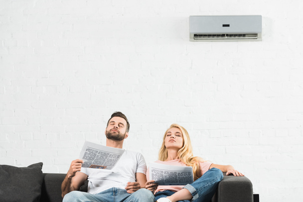 casal no sofá com jornais que sofrem de calor sob ar condicionado em casa
 - Foto, Imagem