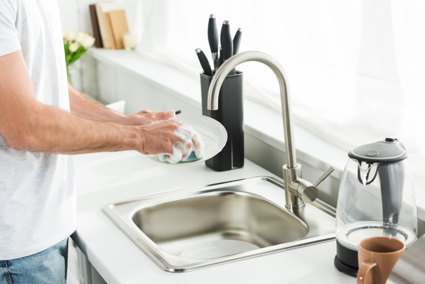 Vue recadrée de l'homme lavant la vaisselle à la cuisine le matin
 - Photo, image