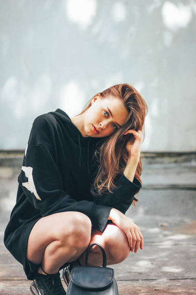 Candid portrait of young beautiful long hair girl fashion model hipster in black hoodie on wall background - Photo, image