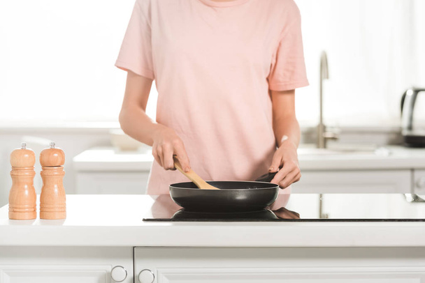 bijgesneden beeld van de vrouw koken met koekenpan en spatel in de keuken in de ochtend - Foto, afbeelding