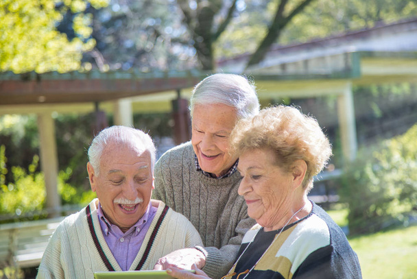 Grupa emerytów korzystających z tabletu w ogrodzie. - Zdjęcie, obraz