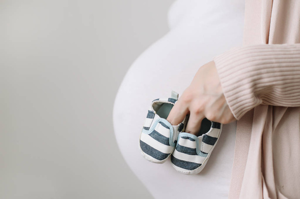 Schwangere mit Babystiefeln in den Händen über dem Bauch. gesunde Schwangerschaft - Foto, Bild