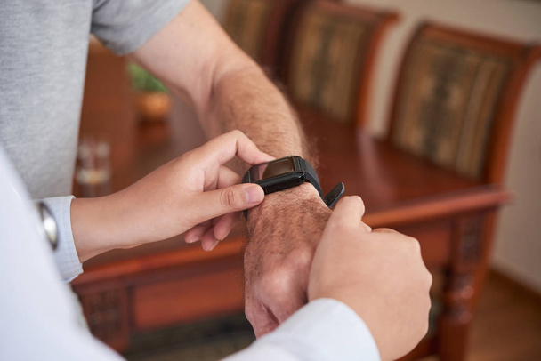 Nahaufnahme eines Arztes, der Gesundheitsapplikation auf Smartwatch am Handgelenk eines älteren Patienten einstellt - Foto, Bild