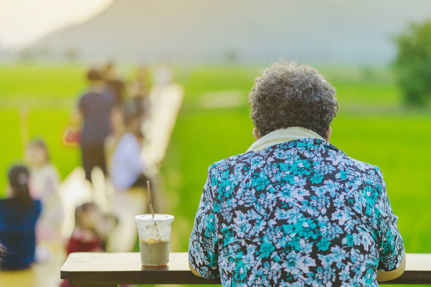 Задний вид пожилой женщины сидеть для отдыха и ждать времени, чтобы сфотографировать закат
  - Фото, изображение