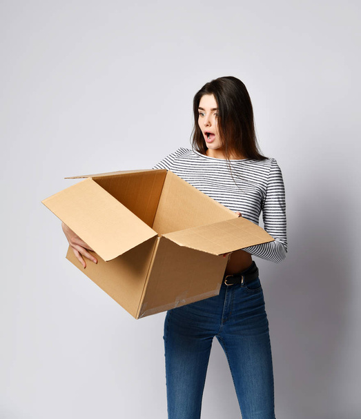 όμορφη μελαχρινή γυναίκα στέκεται σε ένα ελαφρύ φόντο με ένα κινούμενο κουτί από χαρτόνι - Φωτογραφία, εικόνα