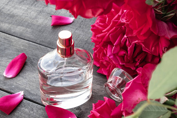 Butelka perfum dla kobiet z czerwonymi róż na tle ciemnych drewnianych desek. - Zdjęcie, obraz