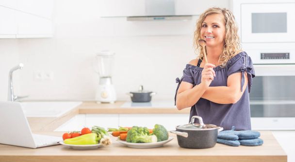Portrait of happy adult woman in her modern kitchen with pot and - Valokuva, kuva