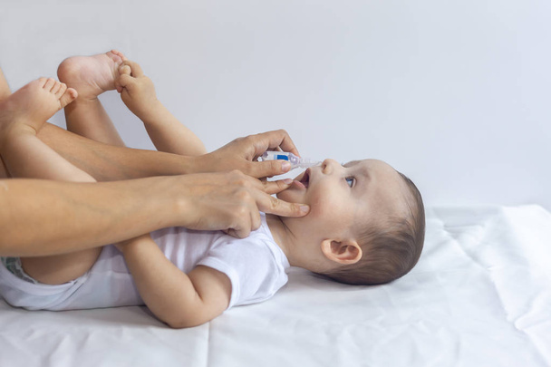 Mały chłopiec coraz krople do nosa. Pediatra wprowadzenie krople soli fizjologicznej w nosie dziecka. Ręce Matki rozliczeń nosa dziecka. 6-miesięczny chłopiec dostaje krople do nosa. - Zdjęcie, obraz
