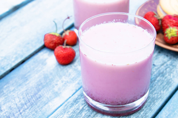 Коктейль с молоком и ягодами в стакане на фоне голубых досок
. - Фото, изображение