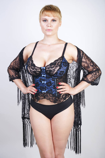 sexy plus size woman with short hair in blue and black lace corset lingerie alone. hot blonde adult girl posing in fashionable underwear on white studio background. - Valokuva, kuva