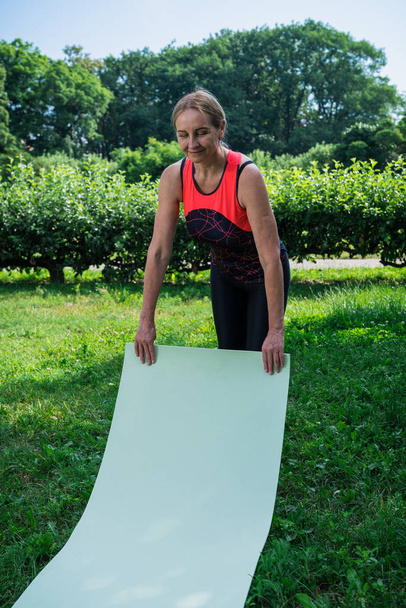 Mujer de 50 años preparándose para practicar yoga en un parque
 - Foto, imagen