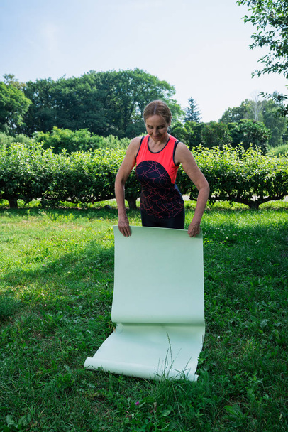 50-летняя женщина готовится к практике йоги в парке
 - Фото, изображение