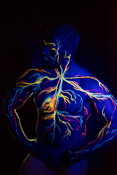 成人男性の体に循環系ボディアートのUV画像。筋肉のアスリートの胸には、静脈や動脈が蛍光色素で描かれています。ネオンライト. - 写真・画像