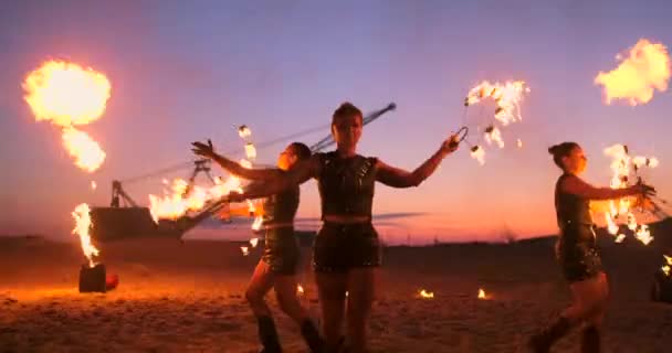 Fire show three women in their hands twist burning spears and fans in the sand with a man with two flamethrowers in slow motion. - Footage, Video