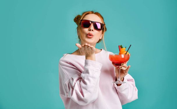 Clubbing young modern woman in fashion sunglasses holds a tropic cocktail strawberry margarita with a orange slice sends a kiss - Foto, Imagem