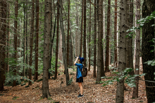 Ormanda dürbünlü ve sırt çantalı genç bir kadın.  - Fotoğraf, Görsel