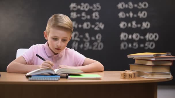 Smart schoolboy solving task, math exercises written on blackboard behind - 映像、動画