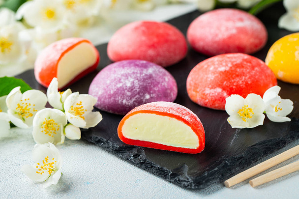 Multi-colored Japanese ice cream Mochi in rice dough and Jasmine flowers on a concrete blue background. Traditional Japanese dessert on a black slate - Photo, Image