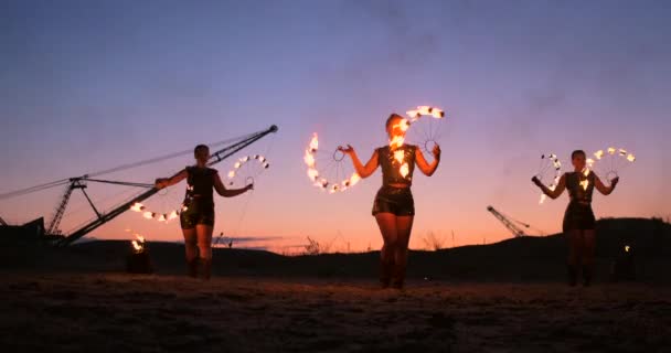 Fire show three women in their hands twist burning spears and fans in the sand with a man with two flamethrowers in slow motion. - Footage, Video