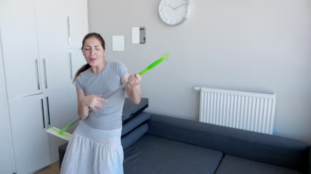 glückliche Frau wäscht Boden mit Wischmopp, singt ein Lied und tanzt in ihrer modernen Wohnung. - Filmmaterial, Video